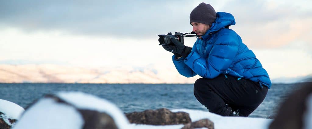 Ett vinterfoto med en man som fotograferar vatten och stenar vid strandkanten.