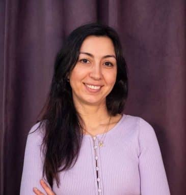 Yasemin Celebio sitter i en grå soffa med en mobil i handen.