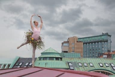 Ballerina dansar på hustak mot en grå himmel.