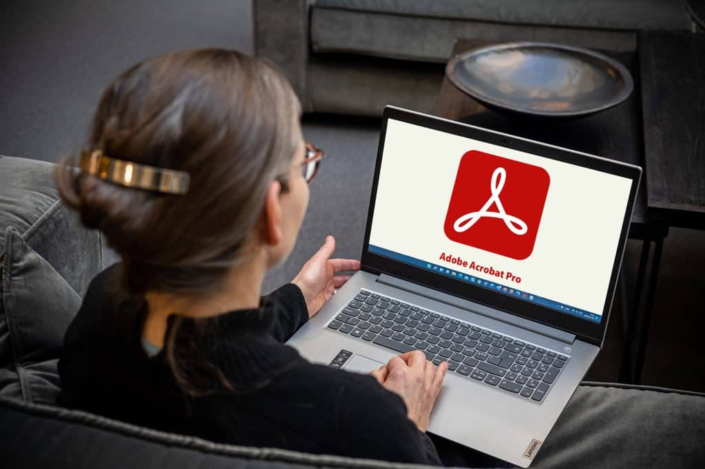 Ulrika sitter i en soffa med sin laptop och loggan för Adobe Acrobat syns på skärmen. Bilden är tagen snett uppifrån.