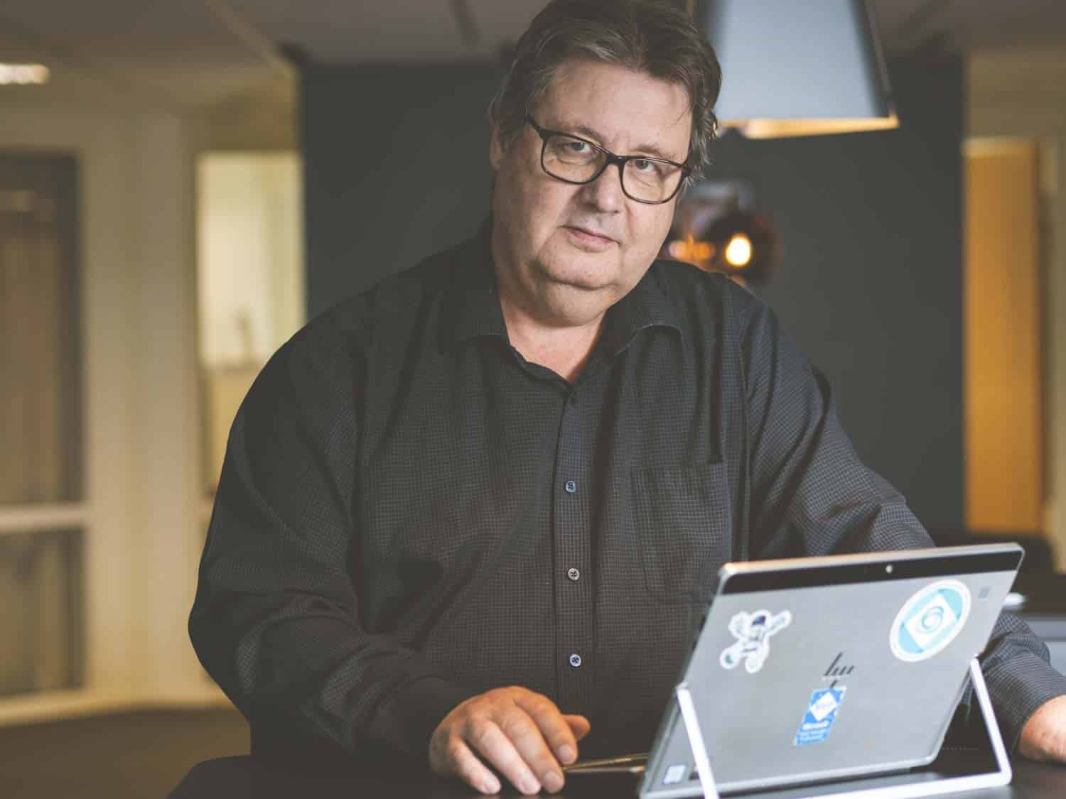 Göran Husman står med sin dator och tittar in i kameran