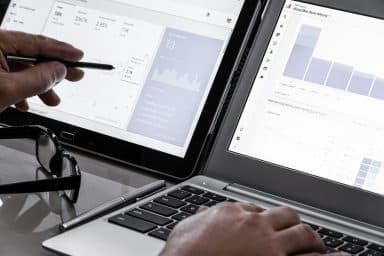 Händer på ett skrivbord med dubbla skärmar som visar Google Analytics