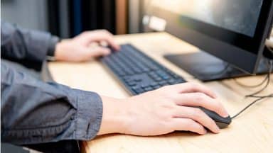 Hand som håller i datormus framför en stationär dator