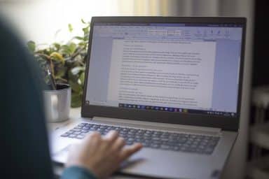 Person som jobbar vid dator. Personens hand syns och datorn har ett Word-dokument uppe.