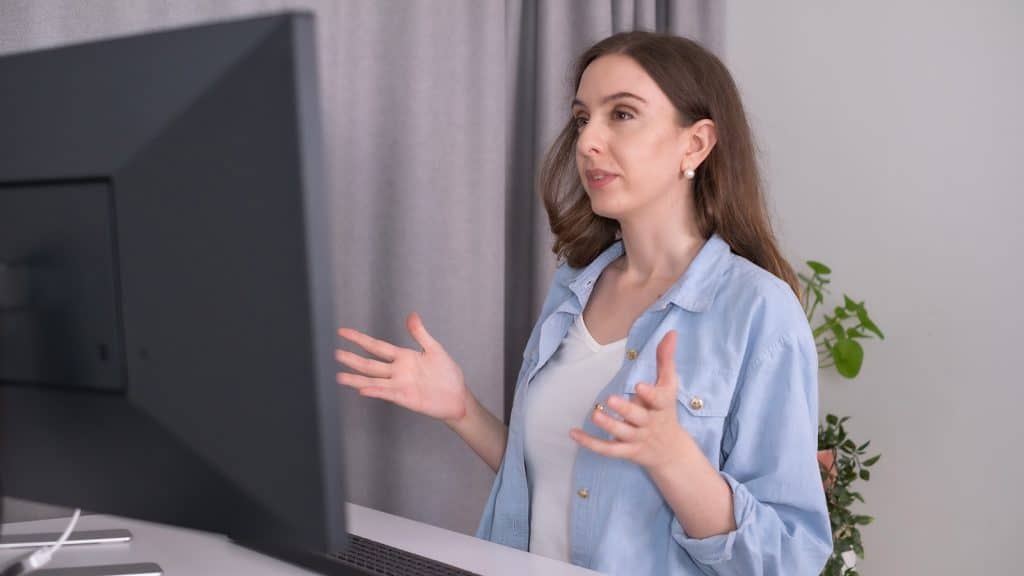 Sabina Chantouria står framför en dator och leder ett digitalt videomöte. Hon tittar mot skärmen och gestikulerar.