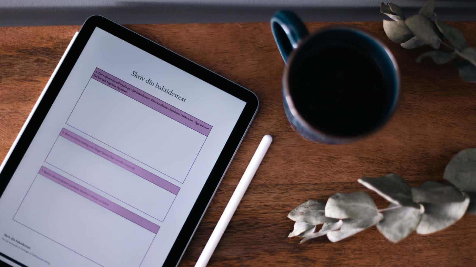 Blå kopp med svart kaffe på ett mörkt träbord. Bredvid ligger en surfplatta med en mall för baksidestext öppen.