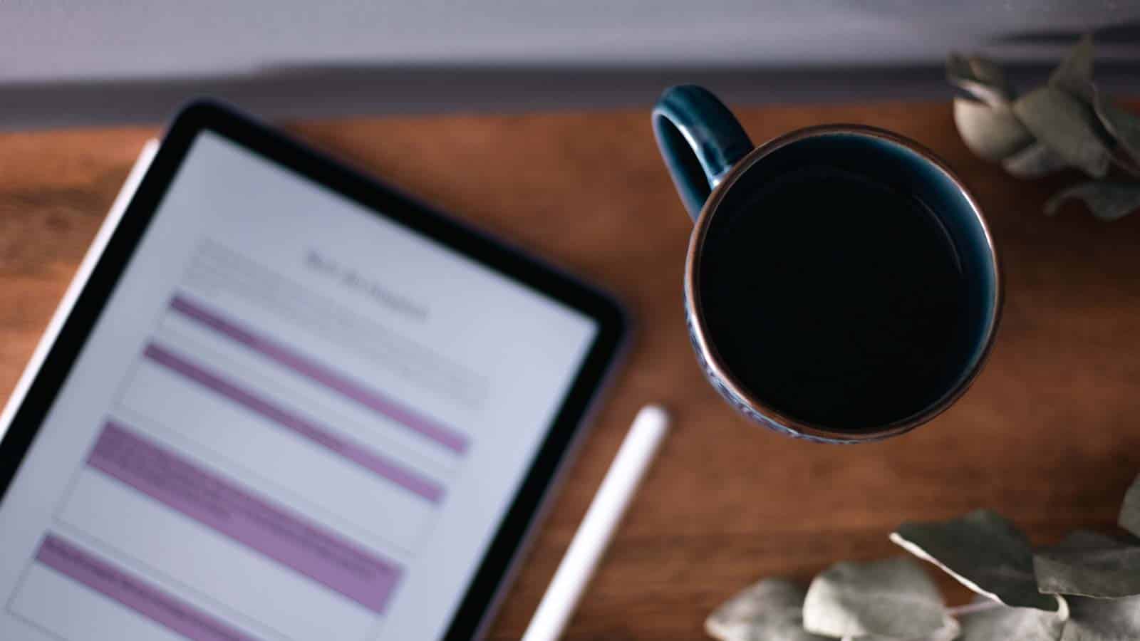 Blå kopp med svart kaffe på ett mörkt träbord. Bredvid ligger en surfplatta med en mall för hisspitch öppen.