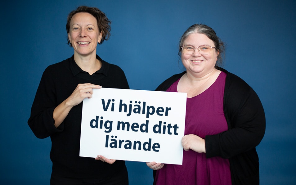 Josefina och Ulrika håller upp en skylt mot kameran där det står 'vi hjälper dig med ditt lärande'