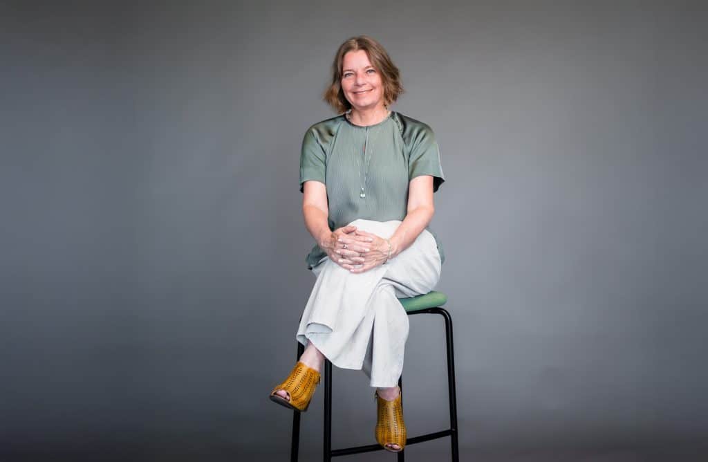 Marie Hemming sitter på en pall och ler mot kameran i en studio.