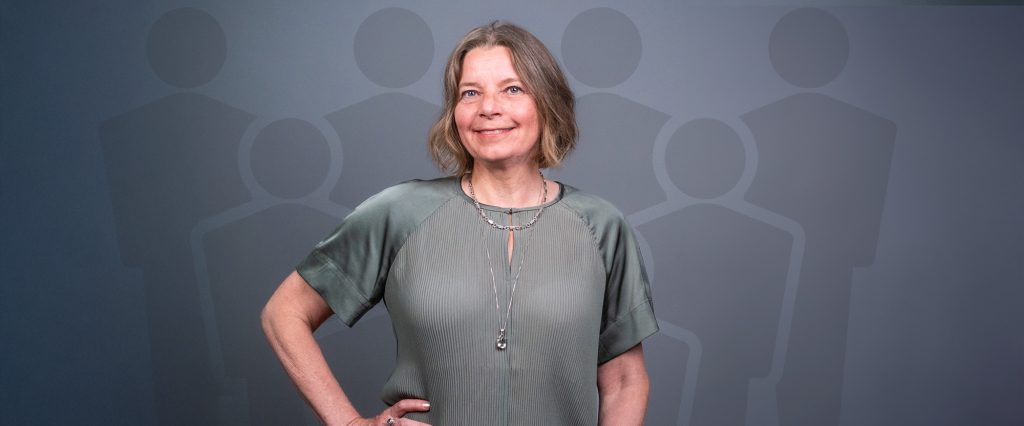 Marie Hemming, lärare i kursen Leda team, ler mot kameran i en trygg pose med ett team illustrerat av ikoner i bakgrunden.