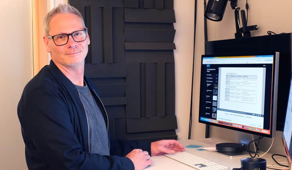 Porträttbild på Mikael Hellman som jobbar med visuell kommunikation på Malmö stad, som står vid sin arbetsplats.