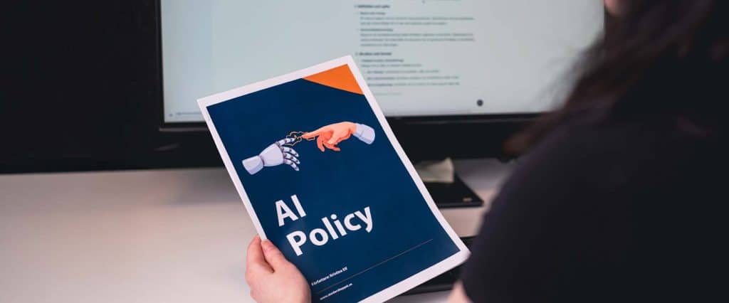 Omslagsbild för onlinekursen AI-policy. Foto av en person som sitter framför en datorskärm och håller i ett dokument med texten
