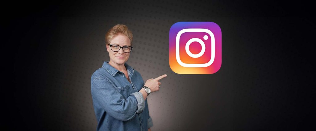 Person i jeansskjorta och glasögon pekar mot en stor Instagram-logotyp mot mörk bakgrund.