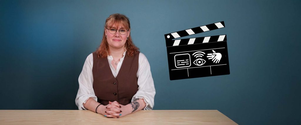 Kvinna sitter vid ett bord framför blå bakgrund. Bredvid henne syns en filmklappa med symboler för undertexter, syntolkning och teckenspråk.