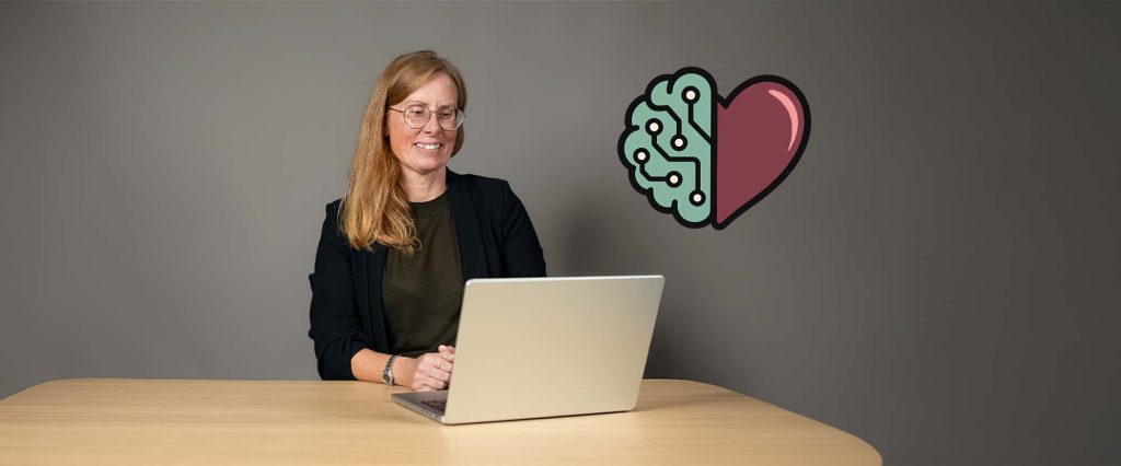 Foto: leende kvinna tittar på en laptop. Bredvid henne syns en illustration där en halv hjärna med kretsmönster sitter ihop med ett halvt hjärta.